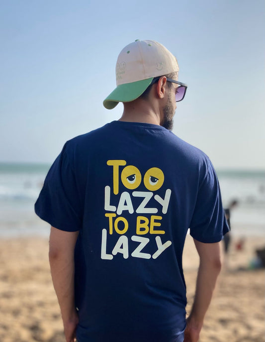 Man wearing a blue t-shirt with 'Too Lazy To Be Lazy' text on a beach